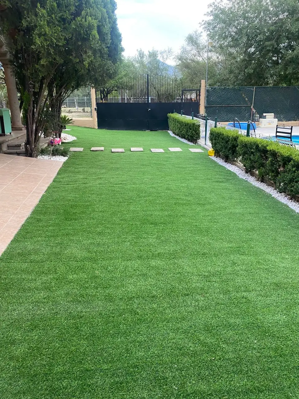 Jardín con pasto sintético, seto y árboles