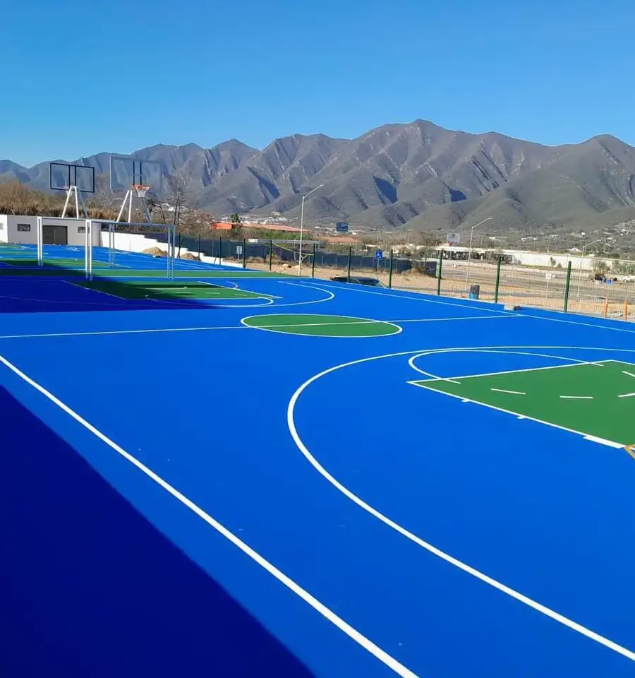 Cancha de básquetbol pintada en azul y verde, con montañas al fondo
